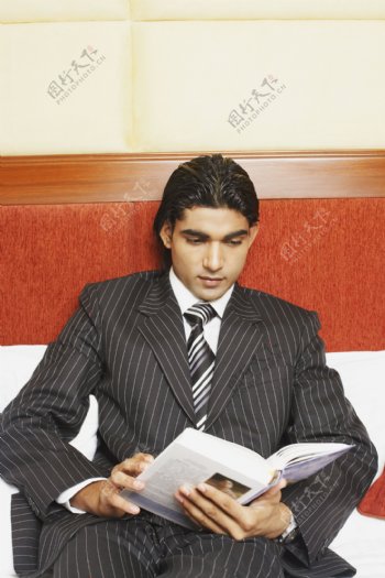穿着西装躺在床上看书的魅力男人图片图片