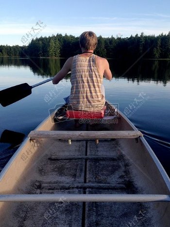 男子布朗背心上艇桨保持在平静的水有了白天绿色高树